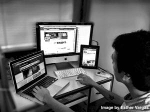 Man sat at desk with computer, laptop and tablet facing him.